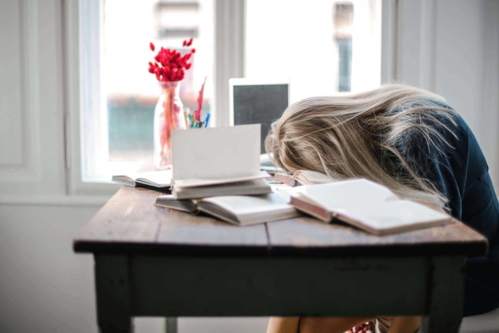 A woman sits at a desk with her head down, appearing to struggle with procrastination.